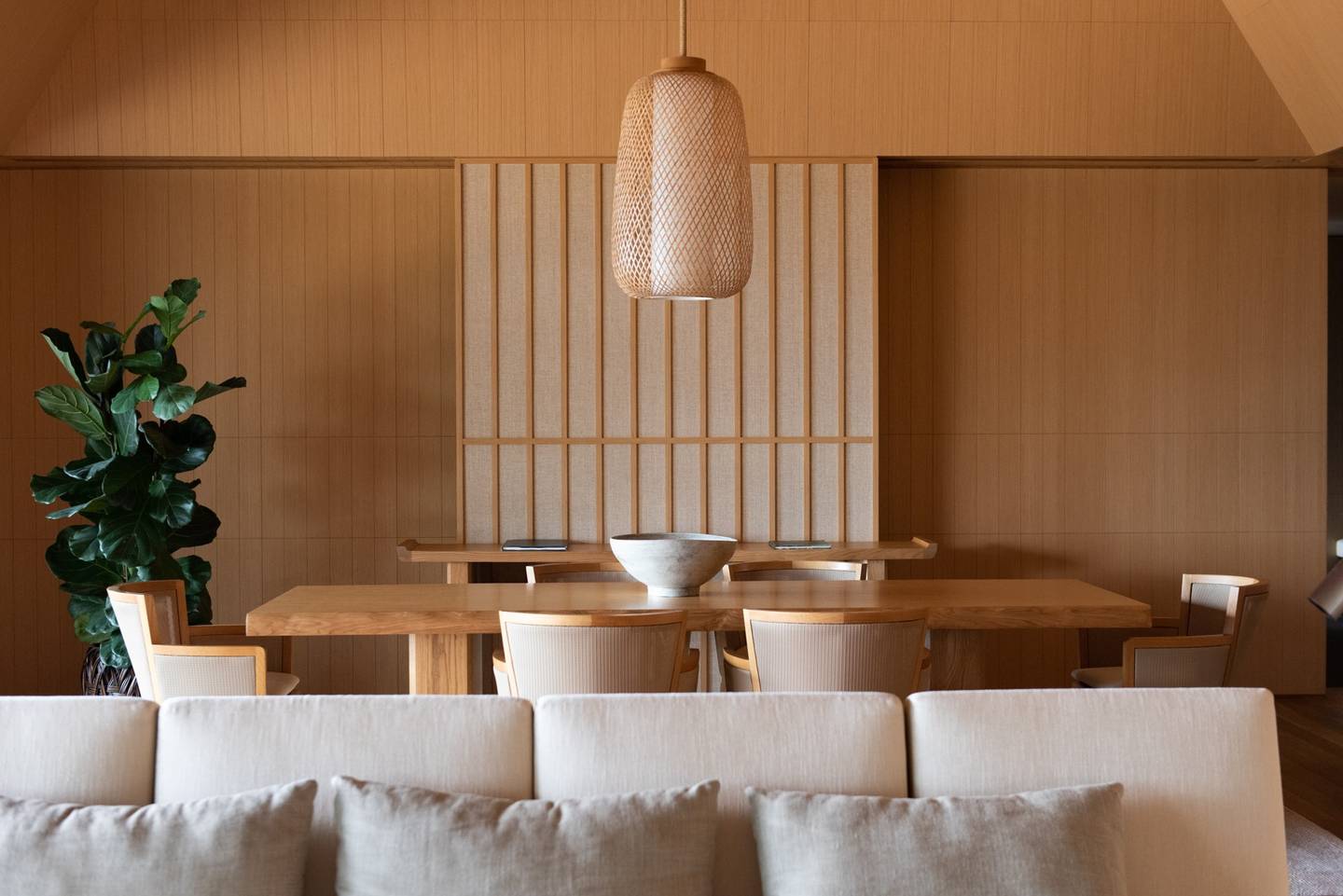 A timber-lined dining room with a woven pendant lamp above a long wooden table